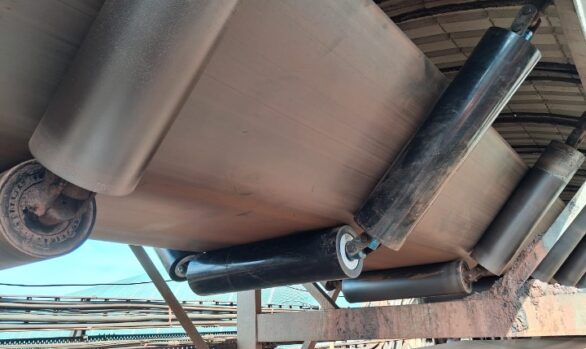Close-up view of a heavy-duty garland roller conveyor system transporting bulk material in the field. The image shows Global polymer idlers supporting a loaded belt